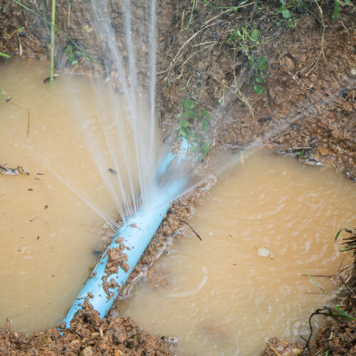 Water Main spraying water from a leak, making puddle in dirt