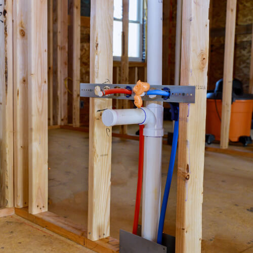 A framed house with a new capped sink drain and red and blue water pipes sticking out of the framing